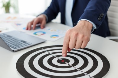 Photo of Man pointing at dartboard at white table indoors, closeup