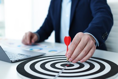 Photo of Man with dart aiming at dartboard while working indoors, closeup