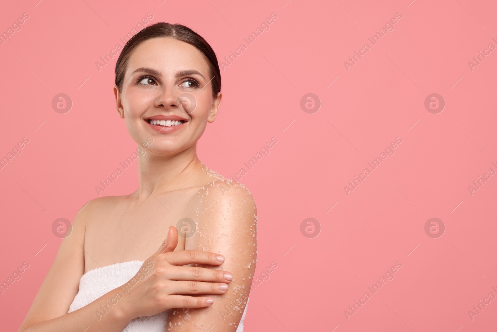 Smiling woman applying body scrub onto her arm against pink background. Space for text Photo of Smiling woman applying body scrub onto her arm against pink background. Space for text