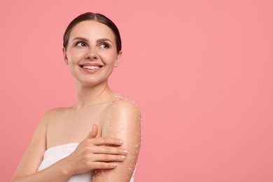 Photo of Smiling woman applying body scrub onto her arm against pink background. Space for text