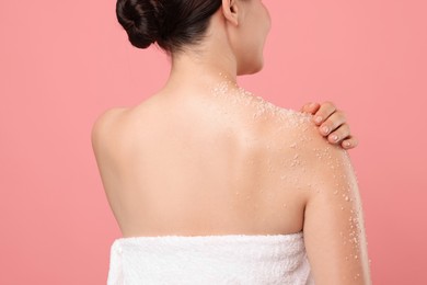 Photo of Woman applying body scrub onto her shoulder against pink background, back view