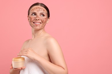 Photo of Smiling woman with body scrub on her face and jar against pink background. Space for text
