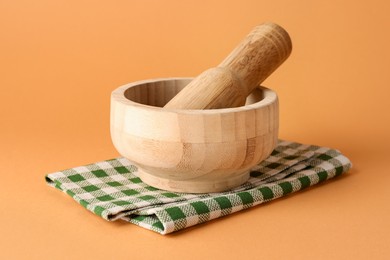 Photo of Wooden mortar, pestle and cloth on light brown background, closeup