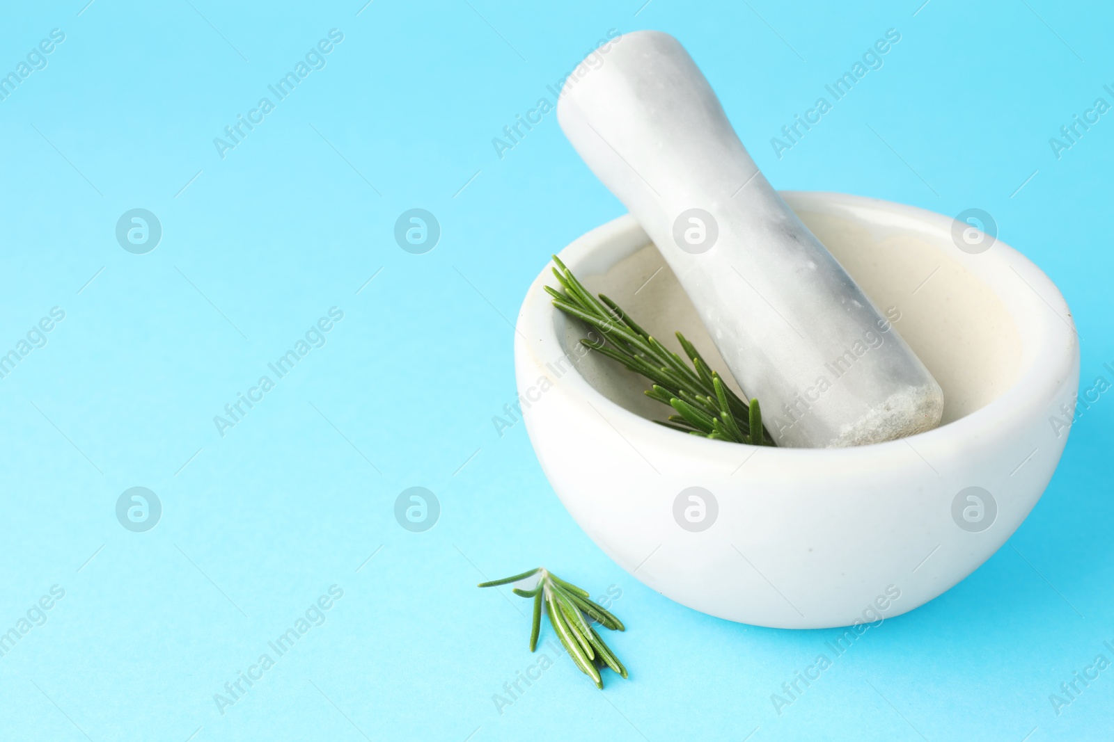 Ceramic mortar with rosemary and pestle on light blue background, closeup. Space for text Photo of Ceramic mortar with rosemary and pestle on light blue background, closeup. Space for text