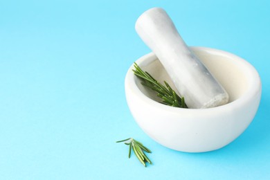 Photo of Ceramic mortar with rosemary and pestle on light blue background, closeup. Space for text