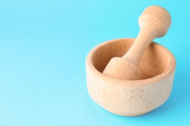 Photo of Wooden mortar and pestle on light blue background, closeup. Space for text