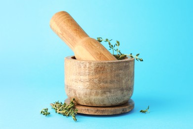 Photo of Wooden mortar with thyme and pestle on light blue background, closeup