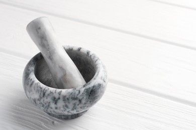 Photo of Marble mortar and pestle on white wooden table, closeup. Space for text