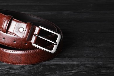 Photo of One brown leather belt on black wooden table, closeup. Space for text
