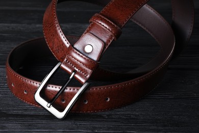 Photo of One brown leather belt on black wooden table, closeup