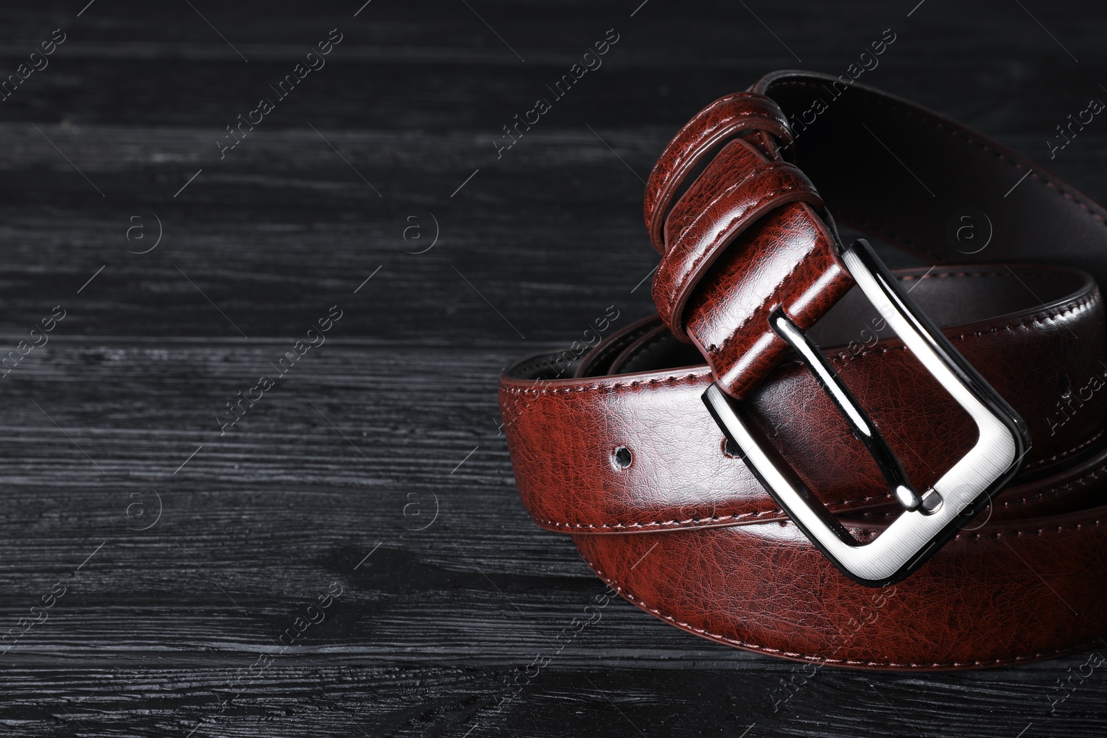 One brown leather belt on black wooden table, closeup. Space for text Photo of One brown leather belt on black wooden table, closeup. Space for text