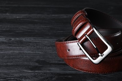 Photo of One brown leather belt on black wooden table, closeup. Space for text