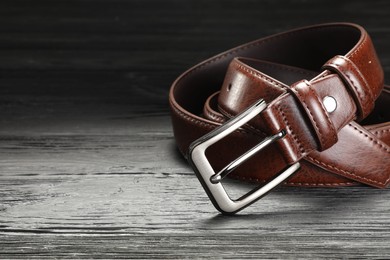 Photo of One brown leather belt on wooden table, closeup. Space for text