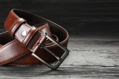 Photo of One brown leather belt on wooden table, closeup. Space for text