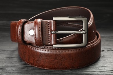 Photo of One brown leather belt on wooden table, closeup