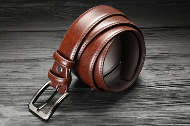 Photo of One brown leather belt on wooden table, closeup