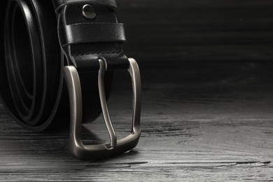 Photo of One black leather belt on wooden table, closeup. Space for text