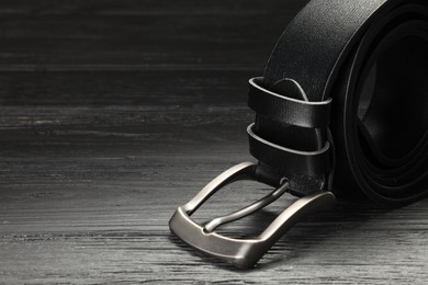 Photo of One black leather belt on wooden table, closeup. Space for text