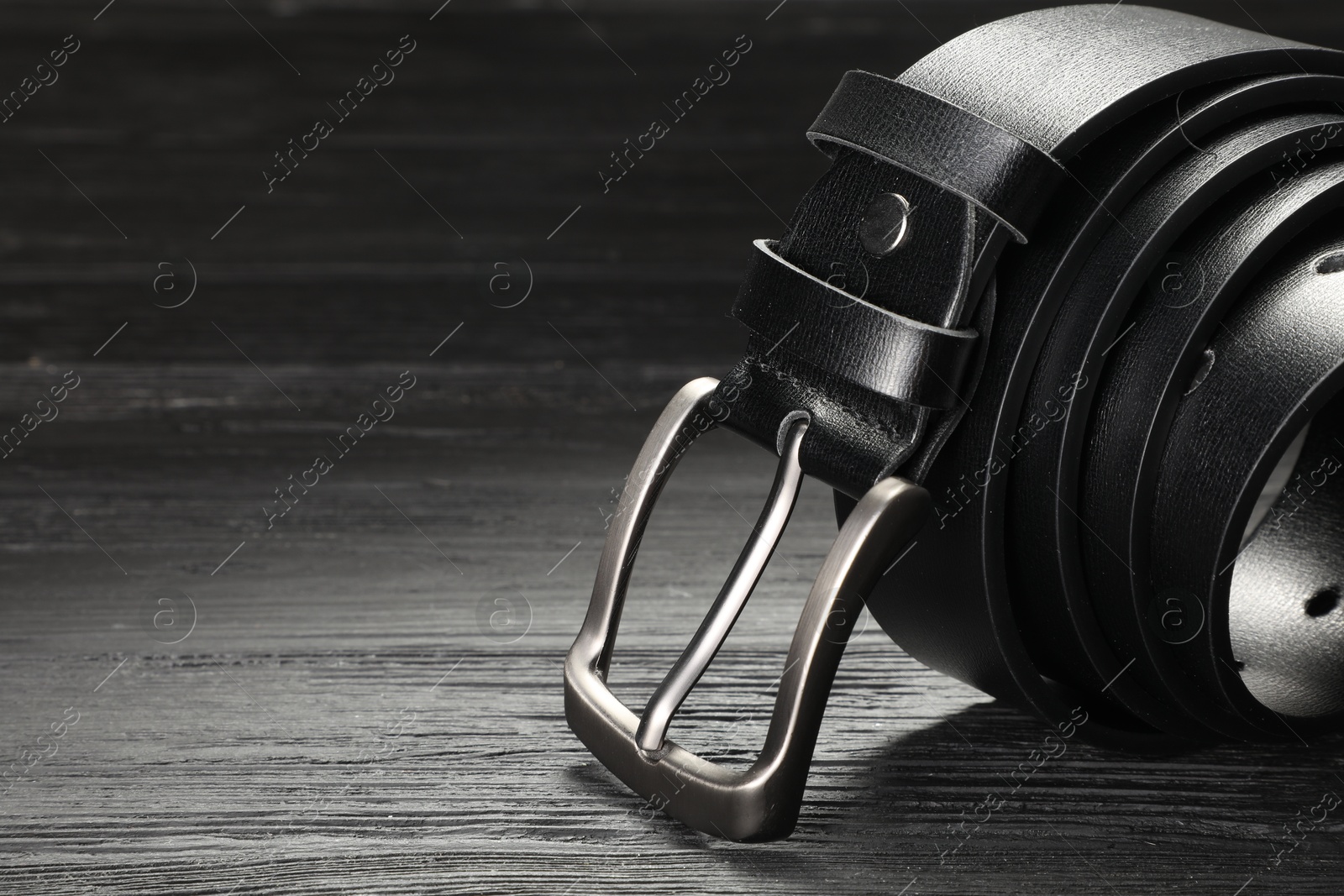 One black leather belt on wooden table, closeup. Space for text Photo of One black leather belt on wooden table, closeup. Space for text