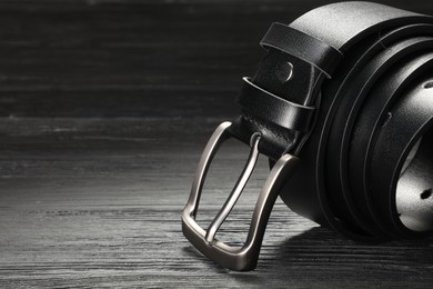 Photo of One black leather belt on wooden table, closeup. Space for text
