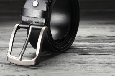 Photo of One black leather belt on wooden table, closeup. Space for text