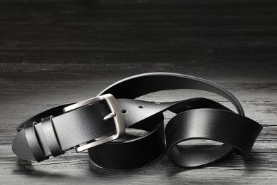 Photo of One black leather belt on wooden table, closeup