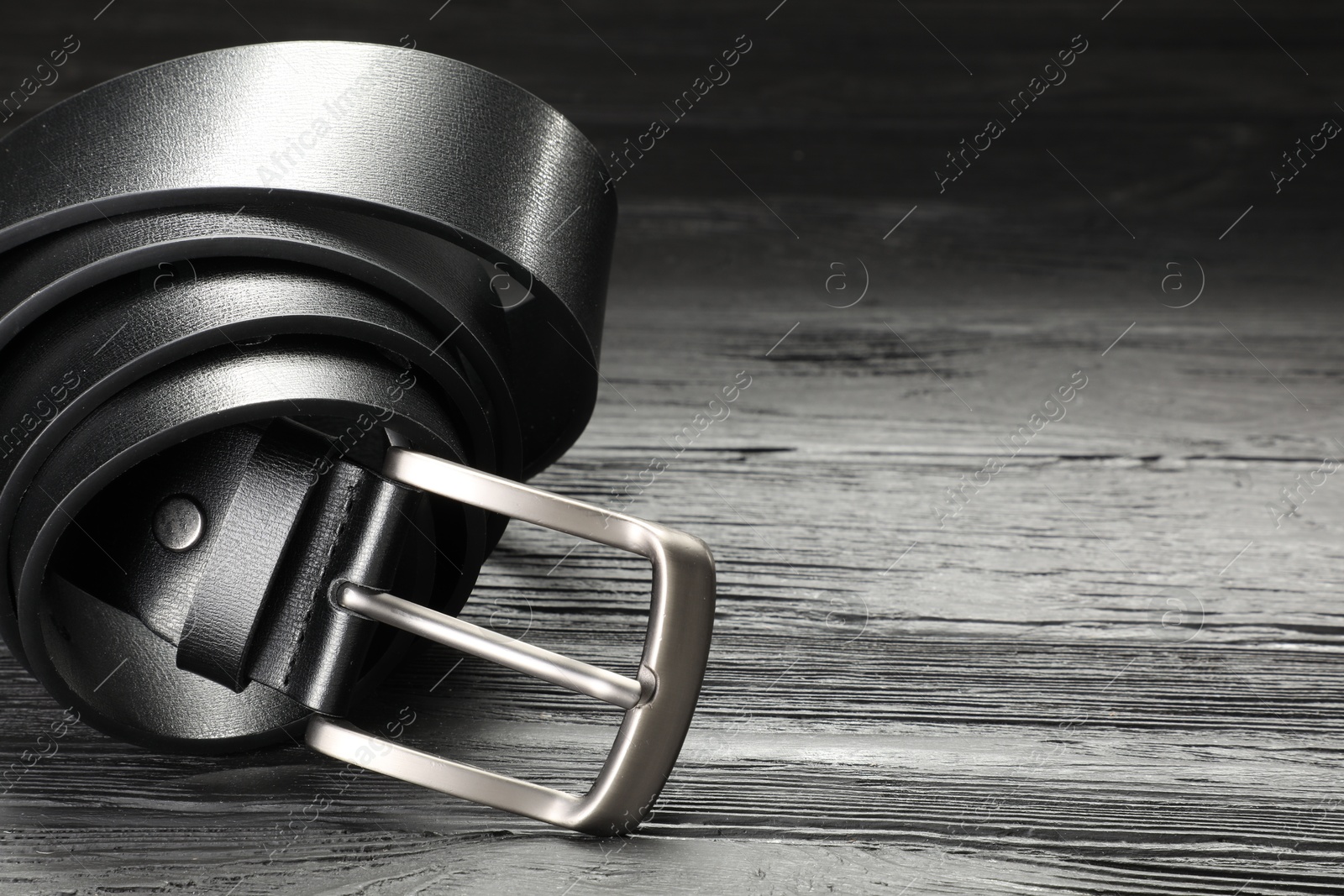 One black leather belt on wooden table, closeup. Space for text Photo of One black leather belt on wooden table, closeup. Space for text