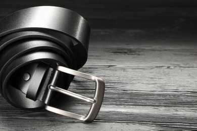 Photo of One black leather belt on wooden table, closeup. Space for text