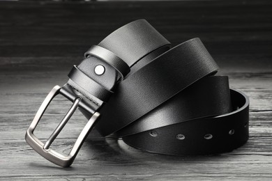 Photo of One black leather belt on wooden table, closeup