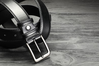 Photo of One black leather belt on wooden table, closeup. Space for text