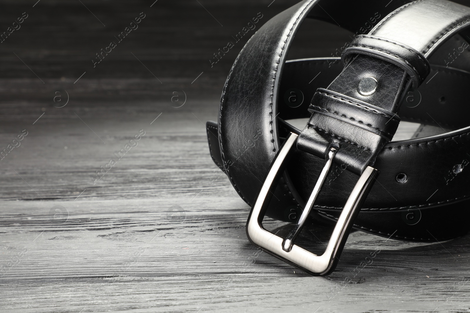 One black leather belt on wooden table, closeup. Space for text Photo of One black leather belt on wooden table, closeup. Space for text