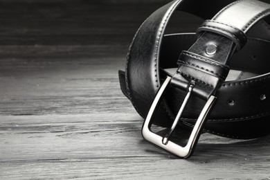 Photo of One black leather belt on wooden table, closeup. Space for text