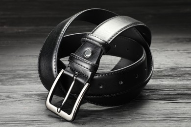 Photo of One black leather belt on wooden table, closeup