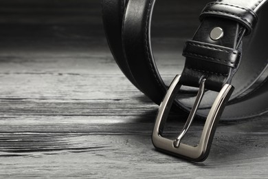 Photo of One black leather belt on wooden table, closeup. Space for text
