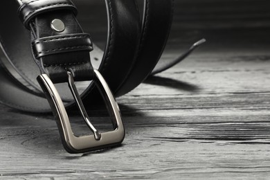 Photo of One black leather belt on wooden table, closeup. Space for text