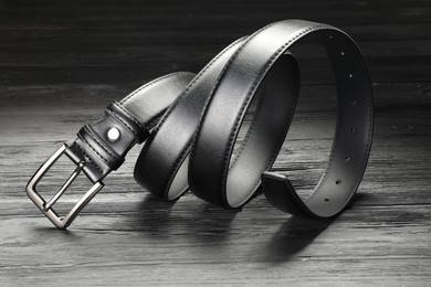 Photo of One black leather belt on wooden table, closeup