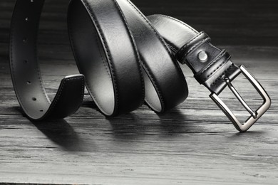 Photo of One black leather belt on wooden table, closeup