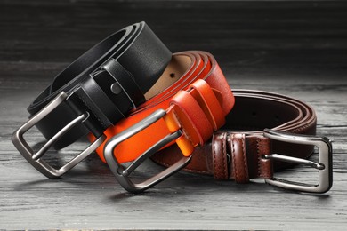 Photo of Three leather belts on wooden table, closeup