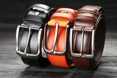 Photo of Three leather belts on wooden table, closeup