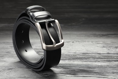 Photo of One black leather belt on wooden table, closeup. Space for text
