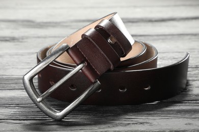 Photo of One brown leather belt on wooden table, closeup