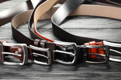 Photo of Many leather belts on wooden table, closeup