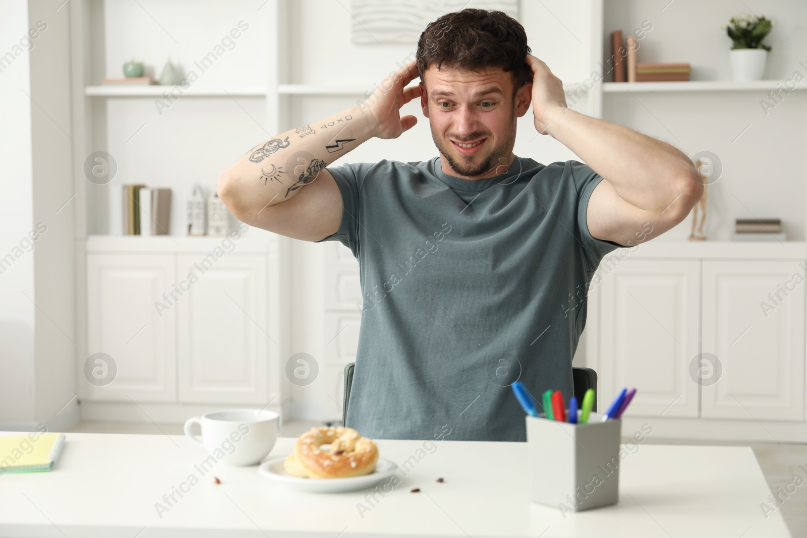 Photo of Shocked young man looking at cockroaches and pretzels on white table indoors. Pest problem