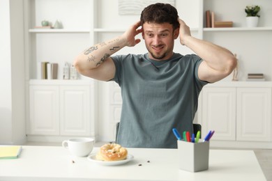 Photo of Shocked young man looking at cockroaches and pretzels on white table indoors. Pest problem