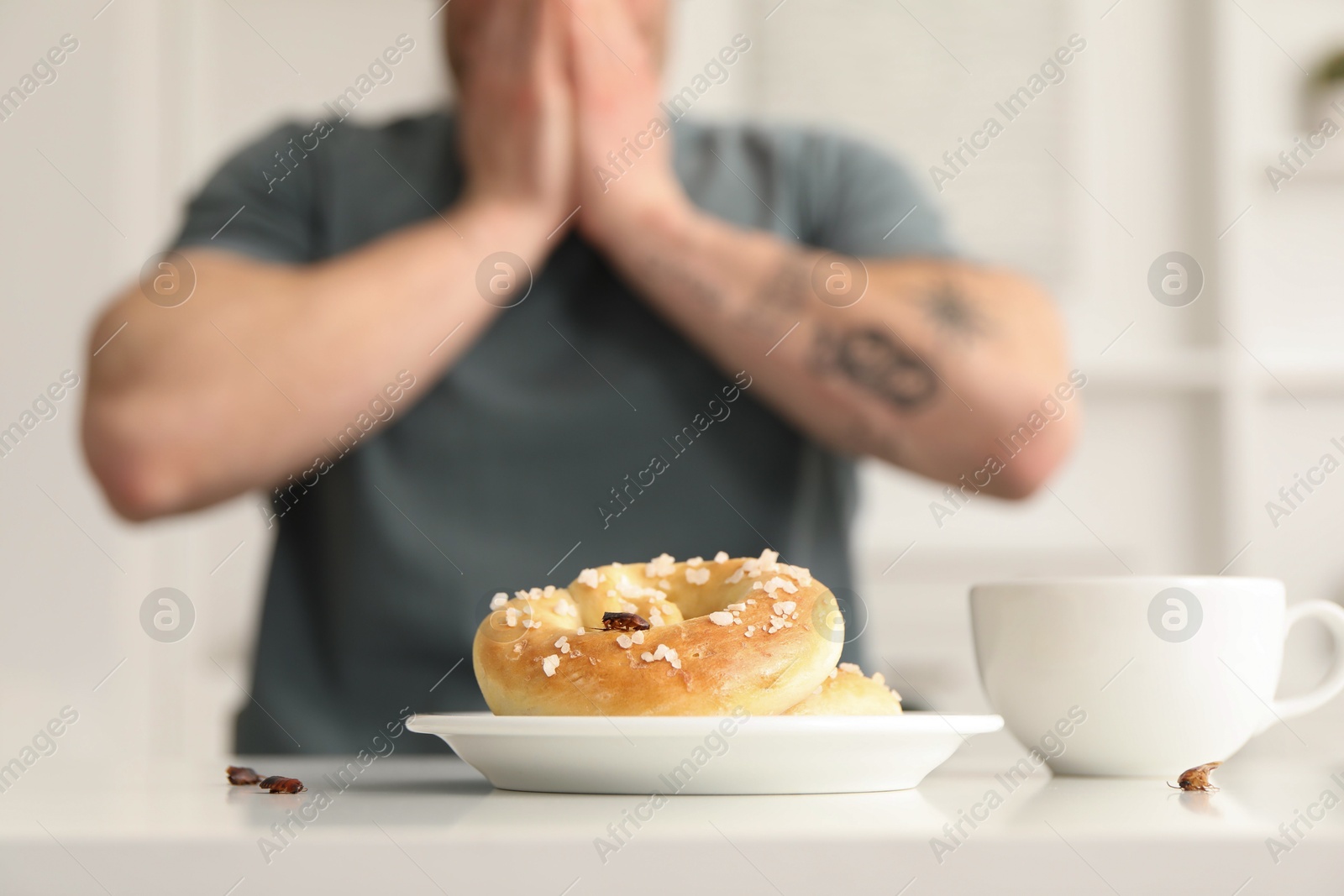 Photo of Shocked young man looking at cockroaches and pretzels on white table indoors, selective focus. Pest problem