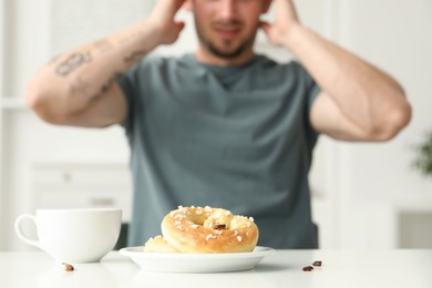 Photo of Shocked young man looking at cockroaches and pretzels on white table indoors, selective focus. Pest problem