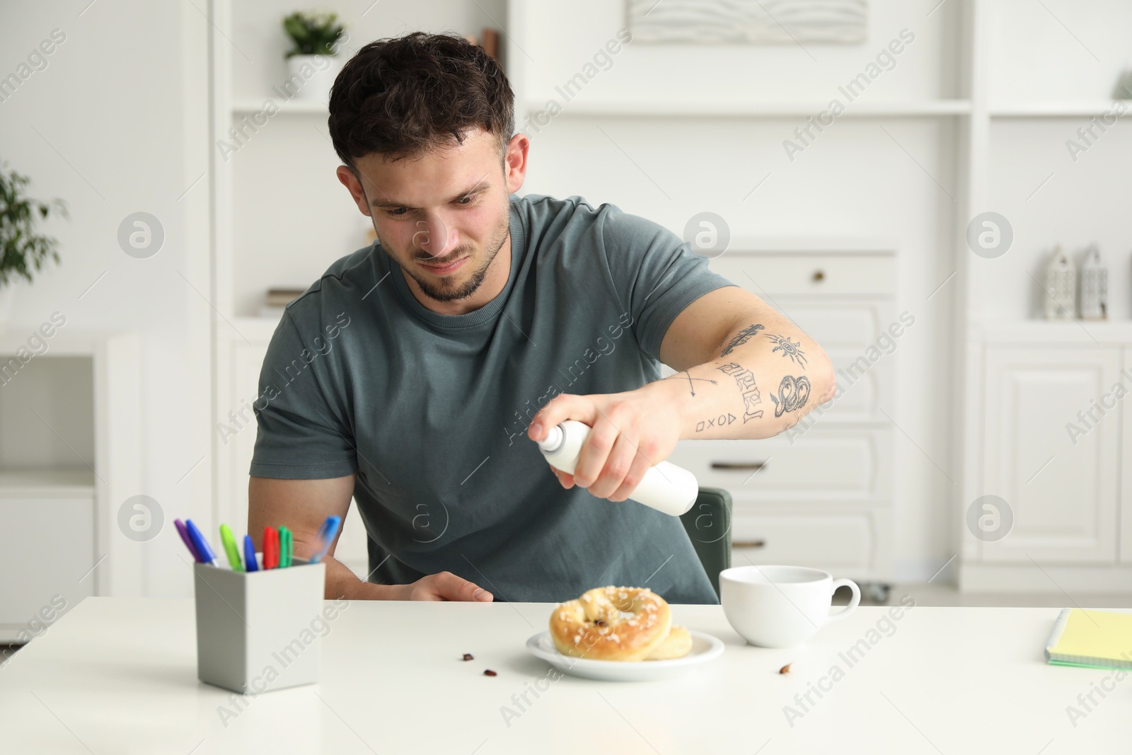 Emotional young man spraying insecticide onto pretzel with cockroaches at white table indoors. Pest problem Photo of Emotional young man spraying insecticide onto pretzel with cockroaches at white table indoors. Pest problem