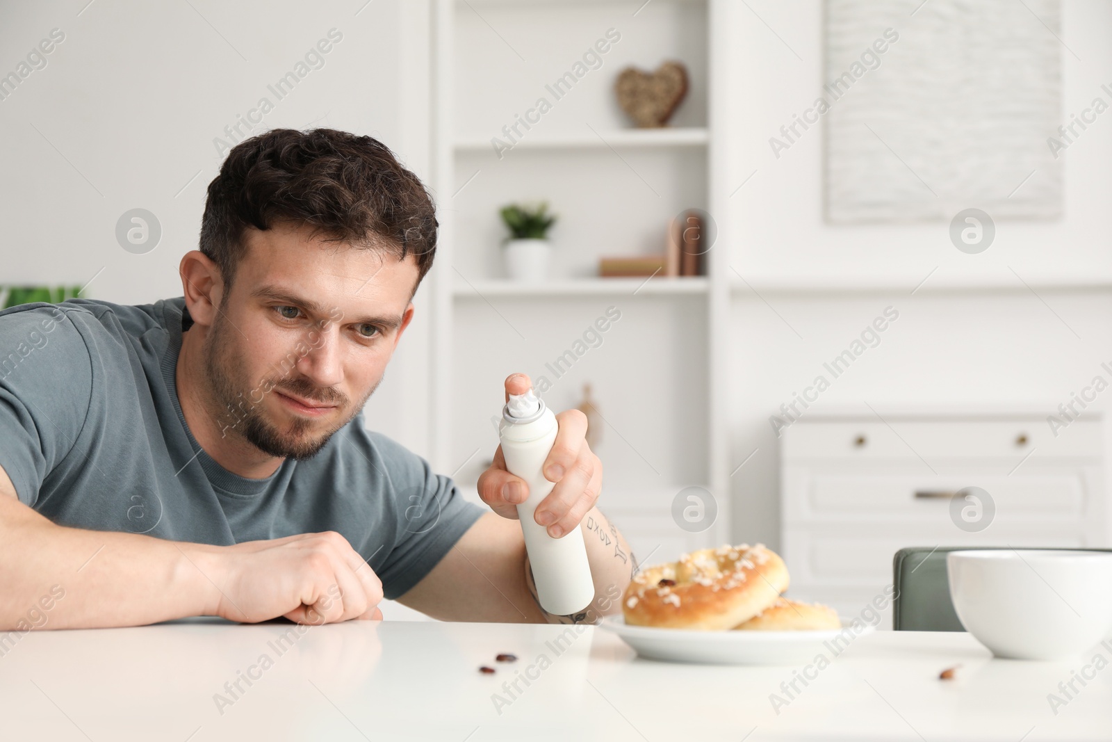 Emotional young man spraying insecticide onto pretzel with cockroaches at white table indoors. Pest problem Photo of Emotional young man spraying insecticide onto pretzel with cockroaches at white table indoors. Pest problem