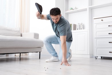 Photo of Emotional young man killing cockroaches with slipper on floor indoors. Pest problem