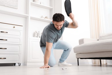 Photo of Emotional young man killing cockroaches with slipper on floor indoors, low angle view. Pest problem